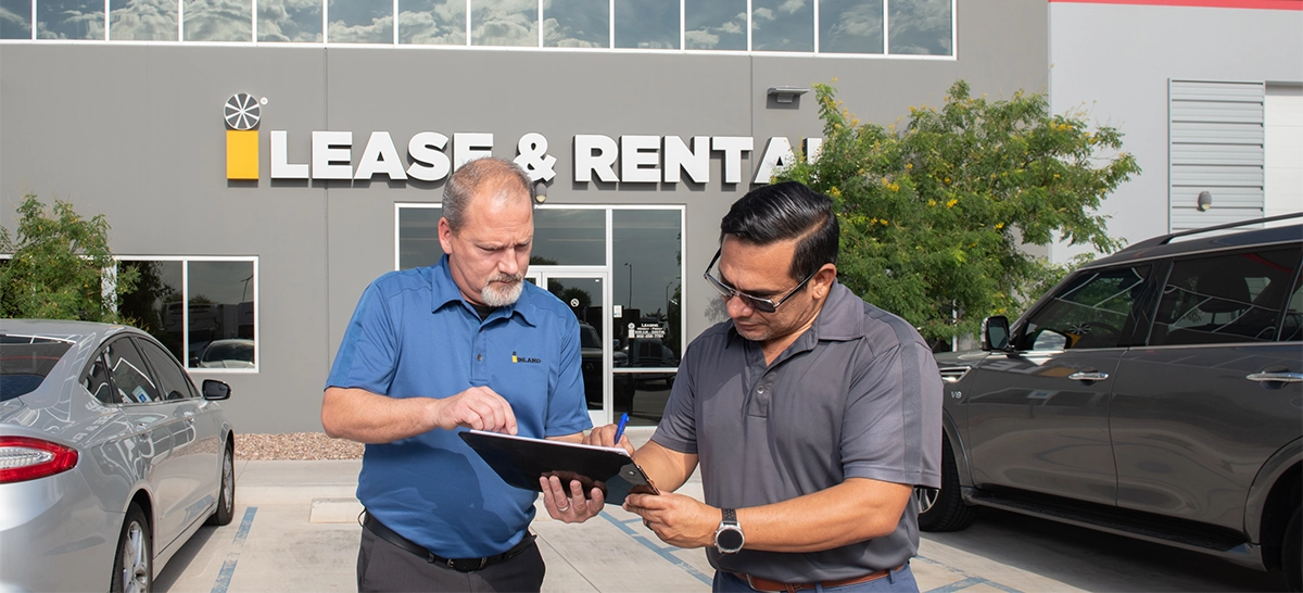 An Inland employee helping a customer complete a semi-truck rental agreement form in front of an Inland Lease & Rental service center.