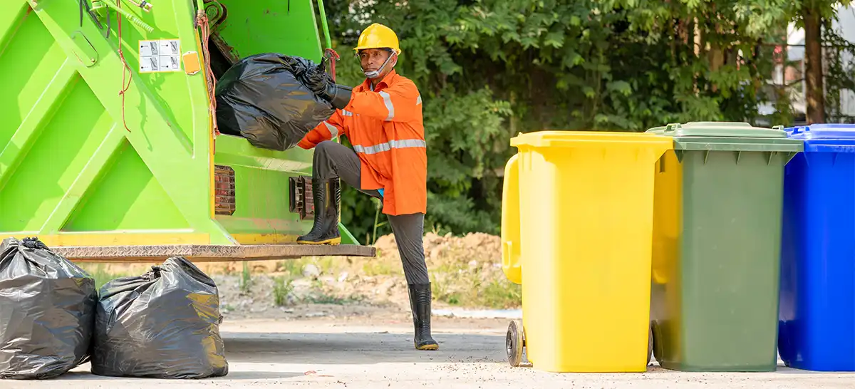 A garbage person throwing a bag of trash into the back of a refuse truck.