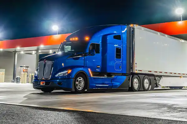 A Kenworth T680 parked at a gas station at night.
